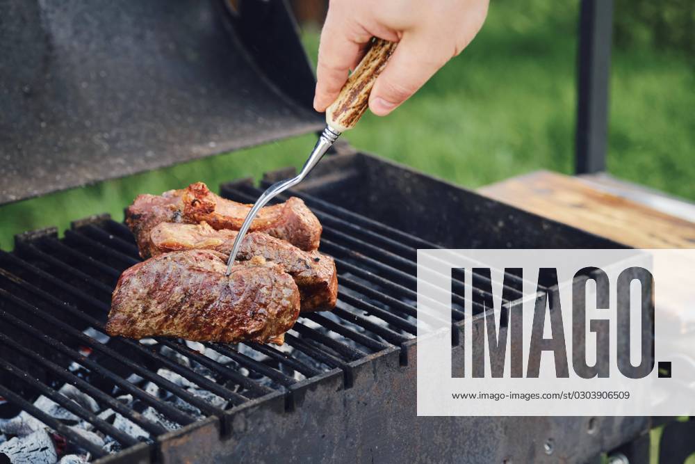 Unbekannter Mann beim Grillen eines Steaks im Freien. Er wendet das Fleisch mit einer Gabel