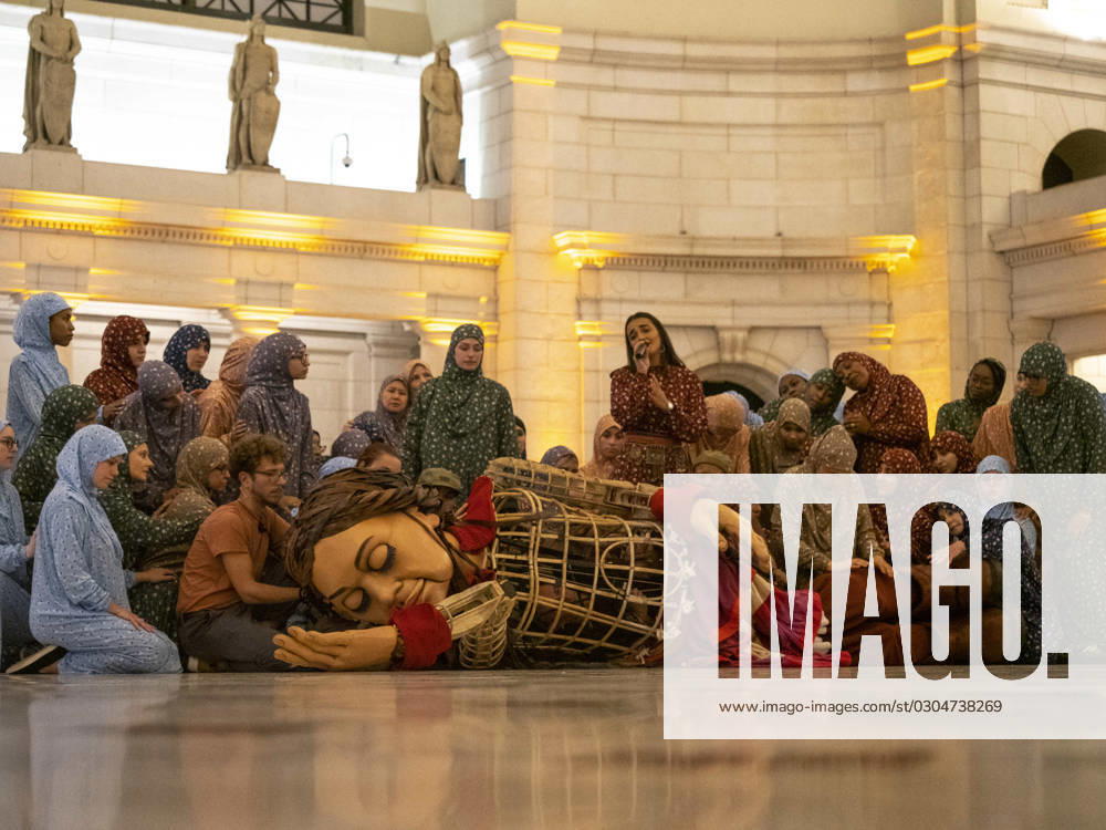 A very tired Little Amal lays down to sleep in Union Station, surrounded by dancers representing women from her village. Amal is a 12 foot puppet of a Syrian refugee girl, who is on a 6000 mile journey across the United States to raise awareness of the needs of child migrants and refugees. Washington USA - ZUMAd155 20230919_znp_d155_036