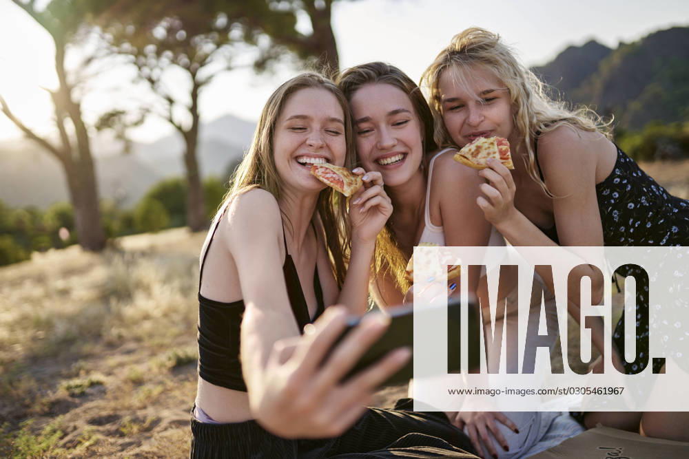 Cheerful young friends having pizza and taking selfie through smart phone model released, Symbolfoto, ANNF00361