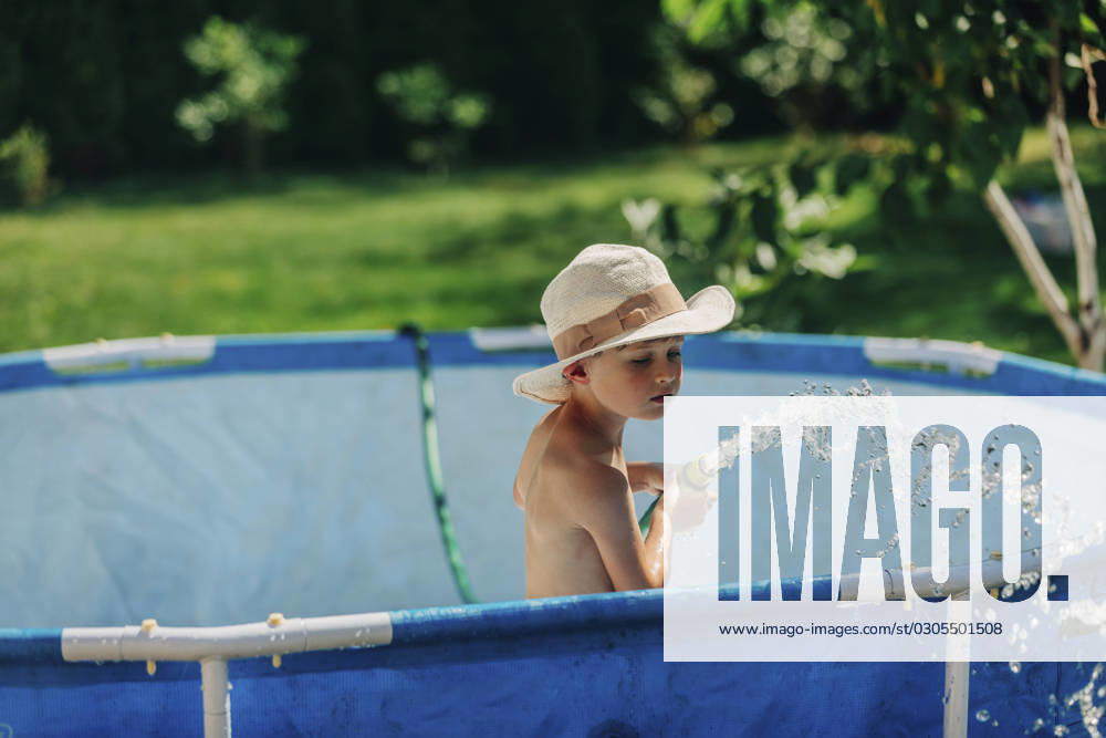 Boy wearing hat playing with water pipe in wading pool on sunny day model released, Symbolfoto, VSNF01330