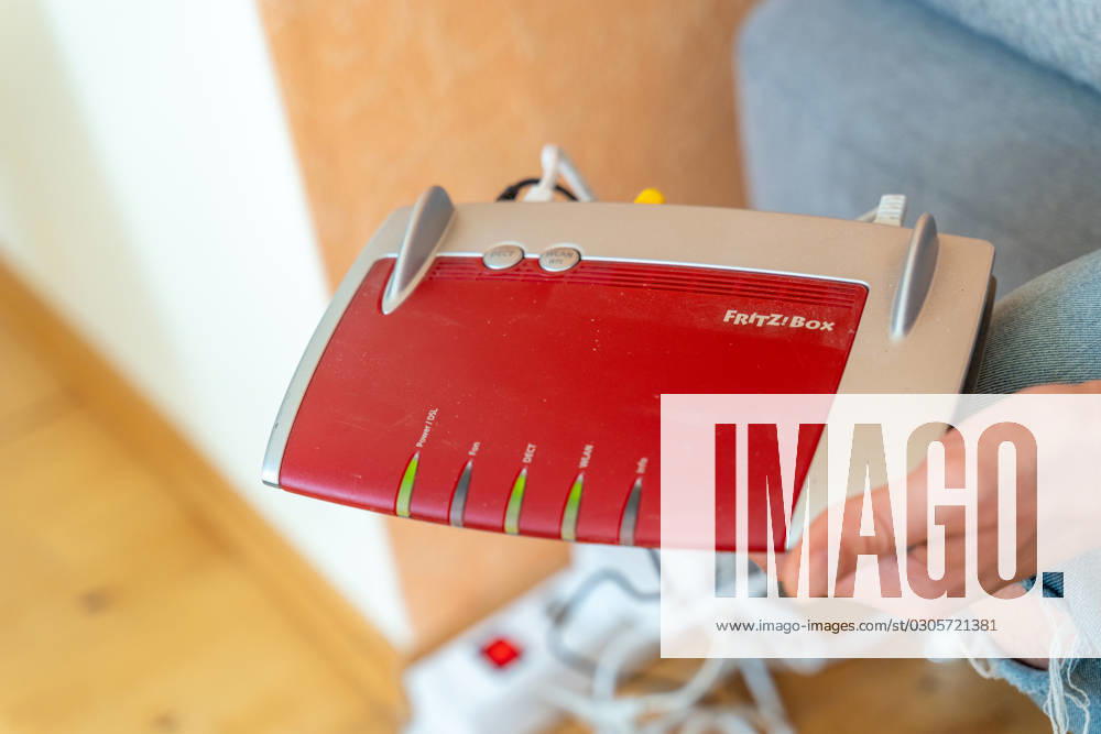Ein Fritzbox Wlan Router in einer Wohnung. Mann hält den Fritz Box Router in der Hand