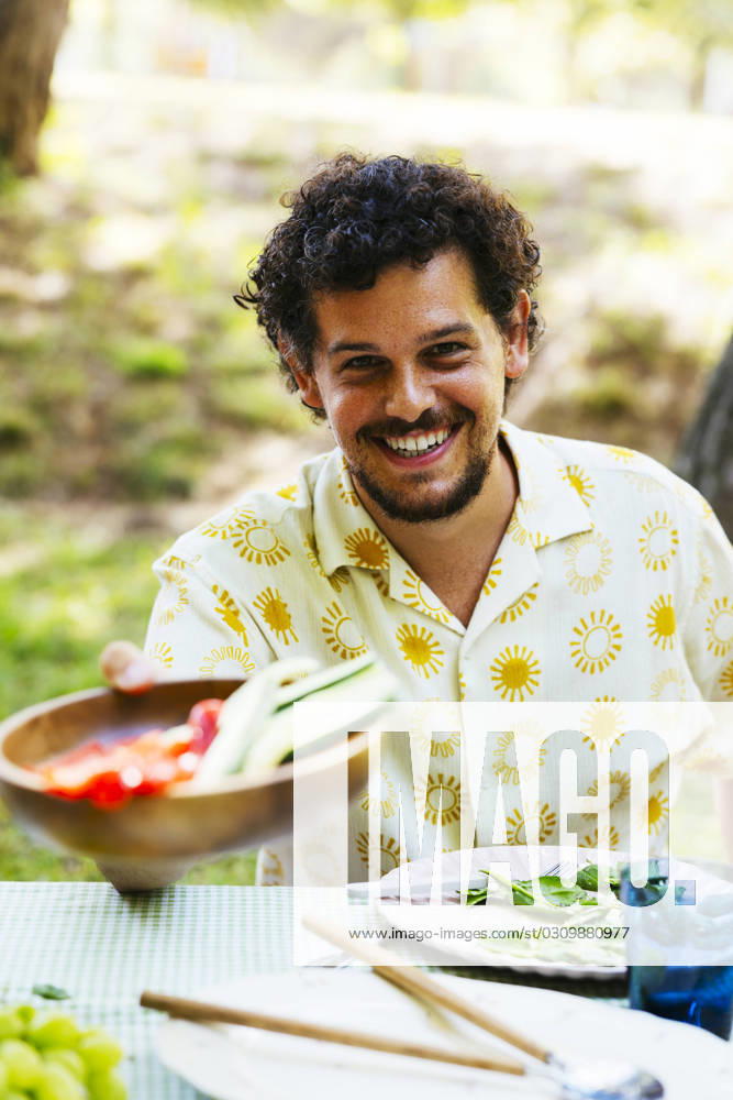 Smiling man offering food at picnic table in garden model released, Symbolfoto, EBSF03751