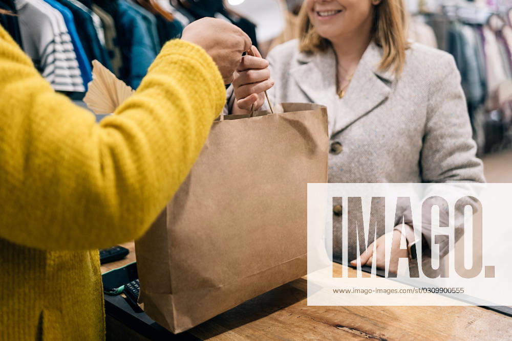 Close-up view of store owner caucasian female hands over a shopping bag to a customer at the checkout counter. Model Released HodeiUnzueta_ID17056_519777_005