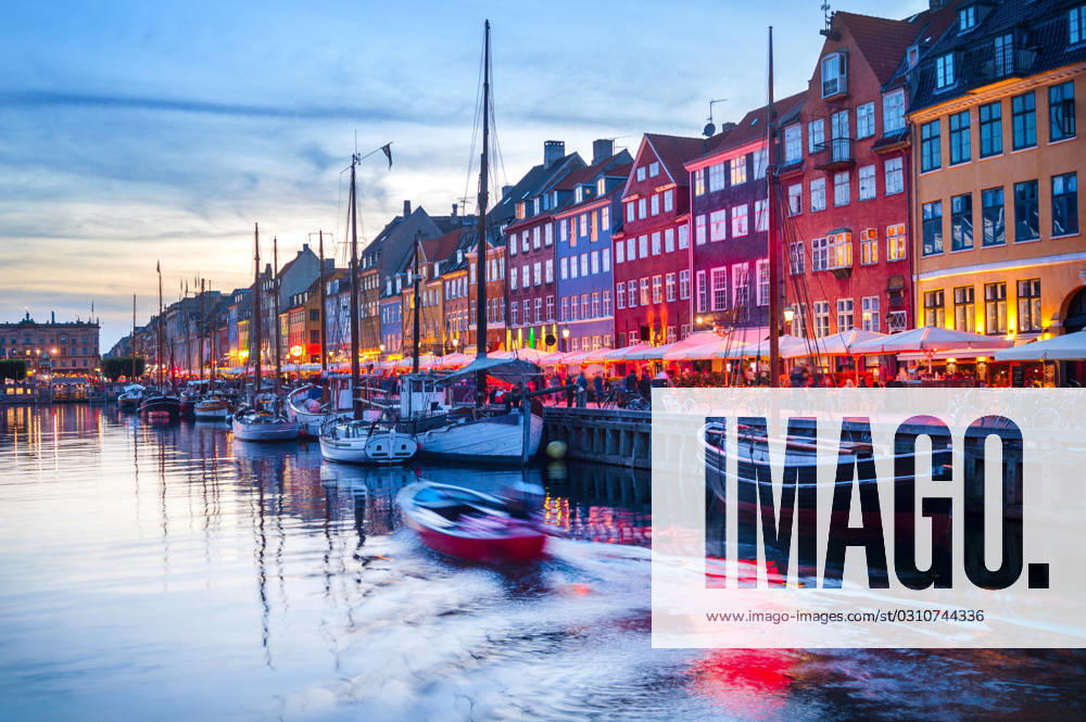 People Nyhavn harbor embankment, Sopenhagen Evening scene with boats moored by illuminated Nyhavn harbor embankment, Copenhagen, Denmark