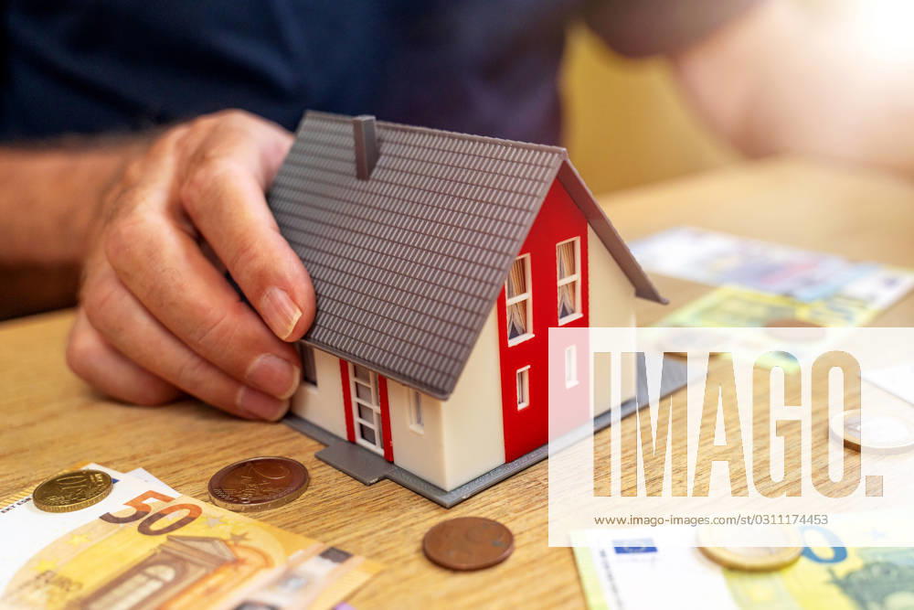 A house is held by an old man in his hand next to euro bills and coins. Real Estate and Finance Concept