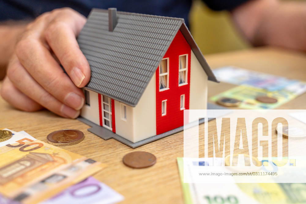 A house is held by an old man in his hand next to euro bills and coins. Real Estate and Finance Concept