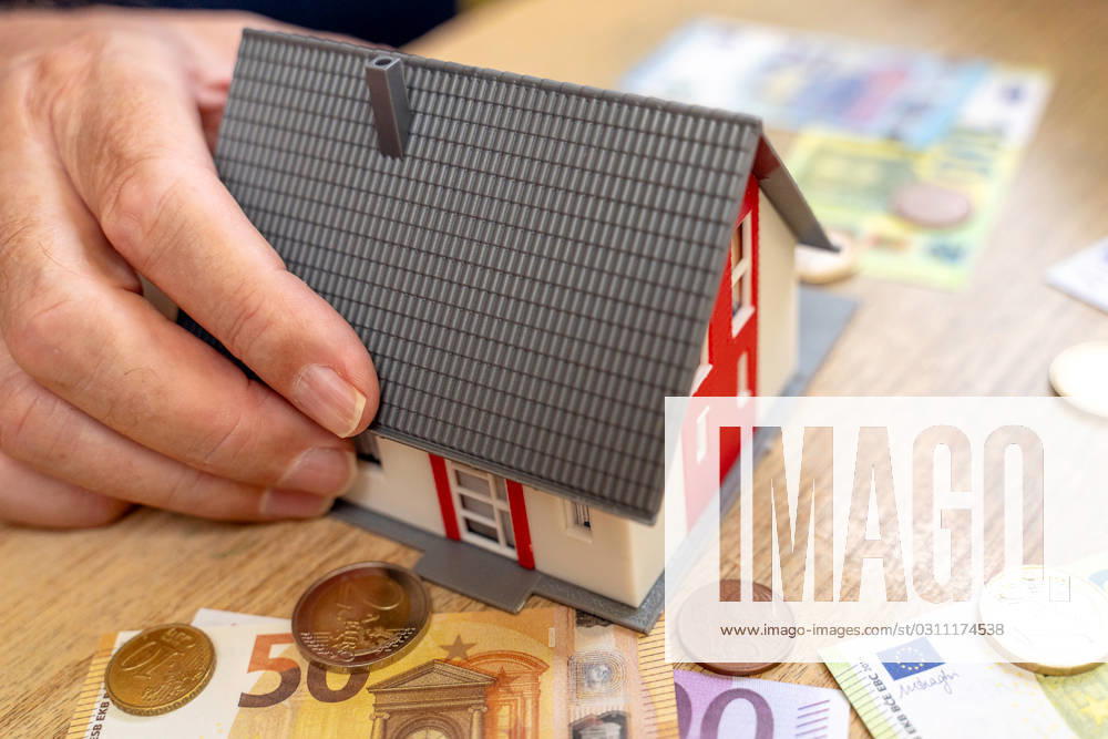A house is held by an old man in his hand next to euro bills and coins. Real Estate and Finance Concept