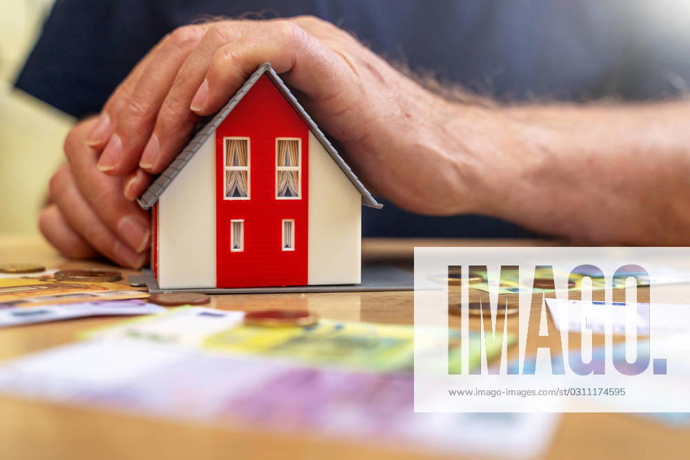 A house is held by an old man in his hand next to euro bills and coins. Real Estate and Finance Concept