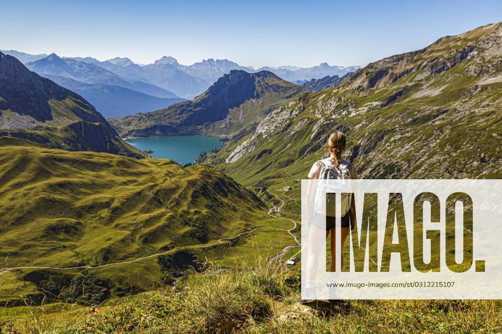 Eine junge Frau steht an einem Wanderweg auf einem Berg und schaut auf den Spullersee in Vorarlberg Lech Östereich