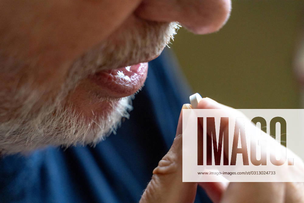 An old man takes a tablet with his mouth open. Disease and medicine concept