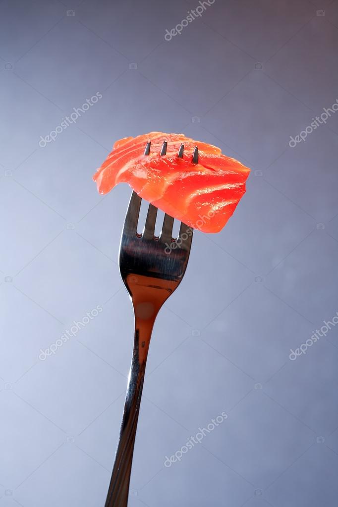 Closeup of steel fork with slice of salmon on dark background