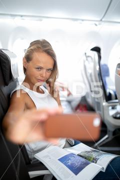 Young happy woman taking selfie photo with passport document sitting on the aircraft seat near a window during the flight in the airplane adult, air, aircraft, airline, airplane, business, cabin, clouds, comfortable, commercial, document, economy, female, flight, fly, girl, happy, holiday, indoor, interior, journey, passenger, passport, people, person, plane, portrait, seat, self, selfie, sitting, tourism, tourist, transport, transportation, travel, traveling, trip, vacation, window, woman, young