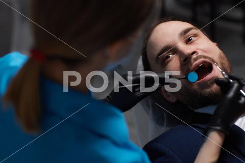 Smiling young man sitting in dentist chair while doctor examining his teeth medical, woman, man, doctor, dentist, tool, specialist, procedure, patient, oral, gloves, examination, health, treatment, clinic, tooth, teeth, dental, medicine, caucasian, equipment, stomatology, visit, mouth, cabinet, checkup, cure, examine, young, uniform, surgical, protective, mask, toothache, latex, operation, hygiene, orthodontist, occupation, dentistry, workplace, indoors, instrument, sterile, heal, hospital, inspection