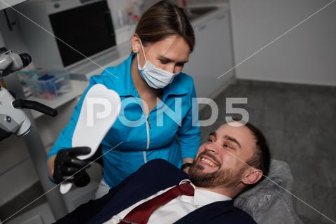 Smiling young man sitting in dentist chair while doctor examining his teeth medical, woman, man, doctor, dentist, tool, specialist, procedure, patient, oral, gloves, examination, health, treatment, clinic, tooth, teeth, dental, medicine, caucasian, equipment, stomatology, visit, mouth, cabinet, checkup, cure, examine, young, uniform, surgical, protective, mask, toothache, latex, operation, hygiene, orthodontist, occupation, dentistry, workplace, indoors, instrument, sterile, heal, hospital, inspection