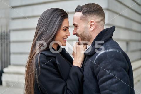 Side view of positive couple in outerwear caressing while standing looking at each other on the street near building during romantic date in city on autumn day couple, love, street, relationship, fondness, date, city, caress, cuddle, romantic, spend time, woman, man, girlfriend, boyfriend, together, soulmate, partner, lover, affection, town, bonding, building, beloved, romance, amorous, in love, gentle, leisure, content, style, glad, trust, amour, tender, positive, valentine, optimist, close, pleasant, spare time, outdoors, looking at each other, smile, happy, delight, side view