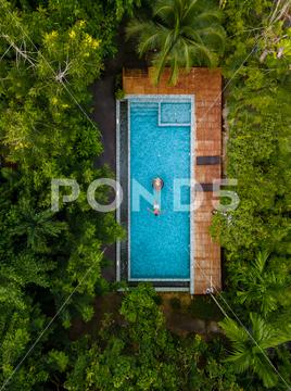 Couple men and woman in swimming pool in the jungle of Krabi Thailand, aerial view with drone above swimming pool in jungle of Thailand. water, blue, drone, vacation, pool, aerial, swim, fun, holiday, travel, tropical, hotel, resort, swimming pool, leisure, man, swimming, people, relaxation, swimwear, top view, outdoor, bikini, girl, woman, nature, top, happiness, sun, sunbathing, sunlight, video, above, lifestyle, aerial view, sea, texture, forest, jungle, landscape, thailand, tree, green, natural, environment, wild, rainforest