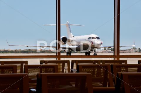 Business plane parked in an airport with seats on foreground. focus on the plane. seat, metal, plane, angled, mode, travel, business, jet, private, vehicle, transport, airplane, blue, airport, air, white, corporate, contemporary, asphalt, commercial, luxury, class, stationary, transportation, sky, upper, space, nobody, horizontal, star, wealth, charter, parked, business, technology, challenger, object, front, sparse, single, road, chassis, wing