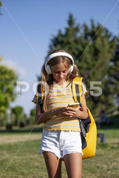 Focused teenage girl with backpack listening to music in wireless headphones while surfing cellphone in park on sunny summer day girl, teenage, smartphone, browsing, online, music, listen, meloman, park, text message, focus, serious, young, scroll, social media, pastime, connection, street, backpack, rucksack, leisure, lawn, summer, headphones, cellphone, playlist, gadget, device, teen, grass, surfing, melody, internet, summertime, kid, song, free time, sound, sunlight, adolescent, chat, audio, outdoors