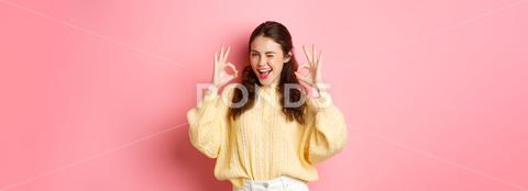 Portrait of cheerful pretty girl winking and saying yes, showing okay sign, alright gesture, praise good job, well done, standing pleased against pink background. student, girl, background, okay, good, approve, alright, agree, yes, praise, woman, advertising, fashion, beauty, person, portrait, grinning, joy, pink, beautiful, joyful, pleased, positive, smile, stylish, studio, horizontal, young, gesturing, glamour, holiday, excited, shopping, isolated, adult, girlfriend, advertisement, casual, smiling, emotive, slim, upbeat, glamorous, cheerful, emotions, excitement, fashionable, brunette