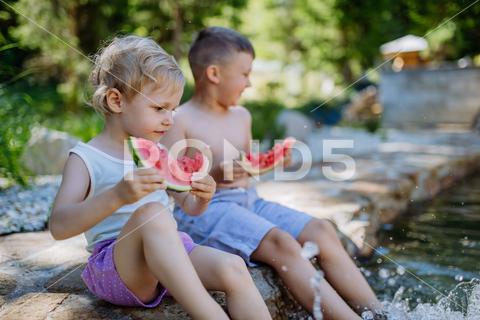 Little chidren sitting near a lake and eating watermelon on hot sunny day during summer vacation. happiness, watermelon, fruit, kid, happy, green, nature, red, food, fun, picnic, healthy, outdoor, joy, health, juicy, eat, girl, childhood, slice, boy, nutrition, cute, sweet, smile, little, eating, cheerful, snack, summertime, caucasian, meal, enjoy, outside, melon, garden, water, delicious, friend, refreshment, holiday, brother, sister, freshness, warm, preschool, siblings