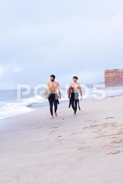 Distant male friends with surfboards and naked torso walking along wet sandy coast near waving sea and looking away men, beach, surfboard, sand, sea, surfer, friend, wave, walk, summer, shore, coast, male, seashore, water, ocean, seaside, leisure, wet, naked torso, tropical, vacation, seacoast, summertime, holiday, shirtless, recreation, hobby, sporty, activity, tourist, seafront, friendship, nature, freedom, seawater, environment, journey, coastline, aqua, waterfront, ripple, calm, stroll, carefree, serene, looking away, distant
