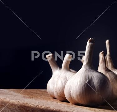 Garlic bulbs on rustic wooden cutting board. still life with dark copyspace. Aromatic food ingredients on kitchen table with black background. Garlic cloves spice prepared for cooking. garlic, food, ingredient, vegetable, spices, still, life, dark, bulb, wooden, background, black, board, clove, cook, copyspace, cuisine, culinary, cutting, diet, dinner, eat, design, flavor, fresh, gourmet, health, healthy, kitchen, medicinal, natural, nutrition, organic, raw, root, seasoning, smell, spicy, table, vegetarian, white, wood, vintage, rustic, head, restaurant, menu, recipe, harvest, onion