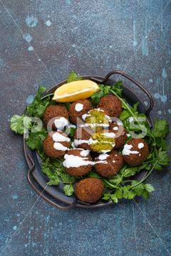 Plate of fried falafel balls served with fresh green cilantro and lemon top view on rustic concrete background. Traditional vegan dish of Middle Eastern cuisine falafel, middle eastern, vegan, plate, vegetarian, fried, food, Levantine, Egyptian, arab, arabian, lebanese, israeli, dinner, meal, dish, table, background, arabic, cilantro, green, fresh, top view, turkish, cuisine, traditional, lemon, organic, tahini, sauce, chickpeas, appetizer, snack, balls, hot, from above