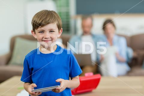 Portrait of smiling boy using digital tablet in living room at home Man, Male, Caucasian, 30s, Mid Adult, Woman, Female, Child, Boy, Chinese, Home, House, Household, Homey, Apartment, Domicile, Abode, Living Room, Casual Clothing, Standing, Smiling, Cheerful, Holding, Using, Web, Internet, Touching, Digital Tablet, Tablet Computer, Tablet Pc, Touchscreen, Wireless Technology, Communication, Connection, Leisure, Lifestyle, Recreation, Authentic, Real Life, Domestic Life, Childhood, Innocent, Innocence, Cute, Adorable, Looking At Camera