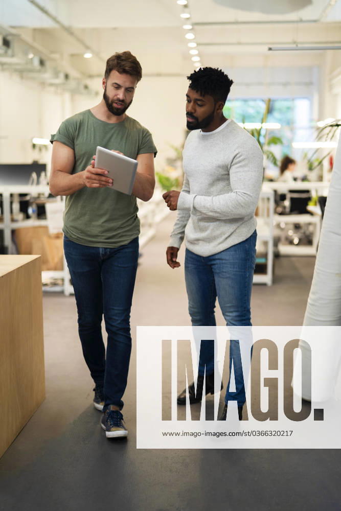 Two coworkers standing while discussing over digital tablet