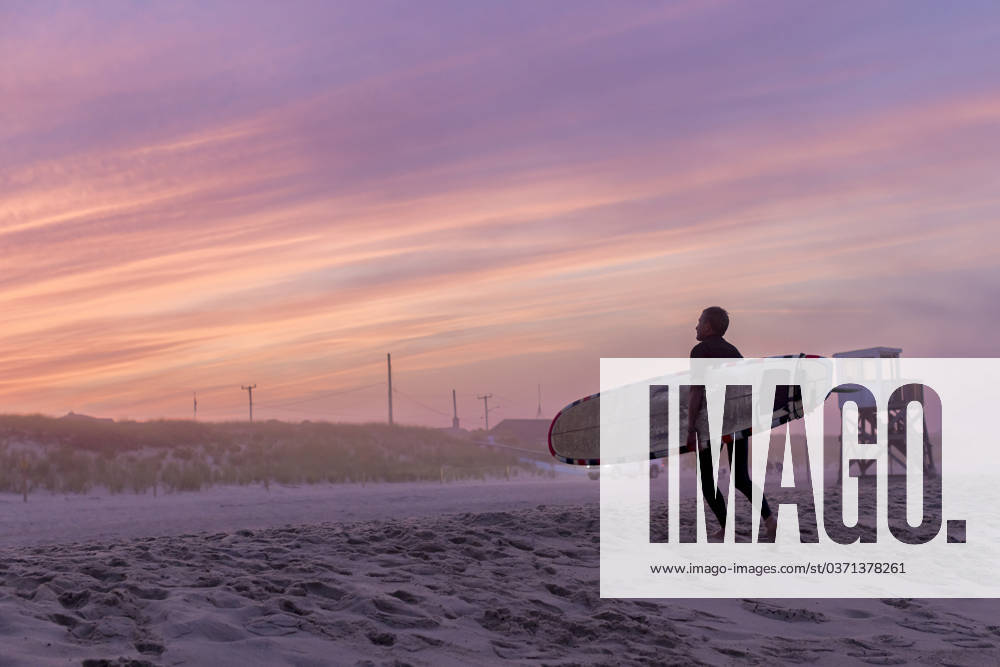 A surfer walks on the beach with his surfboard at sunset Orleans, Massachusetts, United States CR_JUCU231129F1-1272597-01 ,model released, Symbolfoto