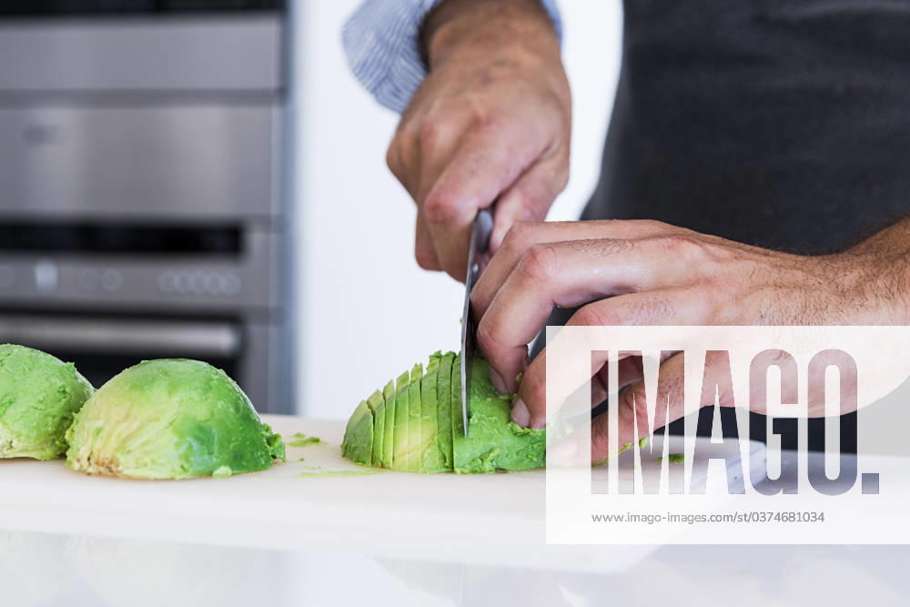 Closeup of crop anonymous private chef in apron cutting avocado with knife while preparing healthy vegetarian breakfast in light kitchen Model Released MartinZubiriaPhotography_ID17004_518467_012