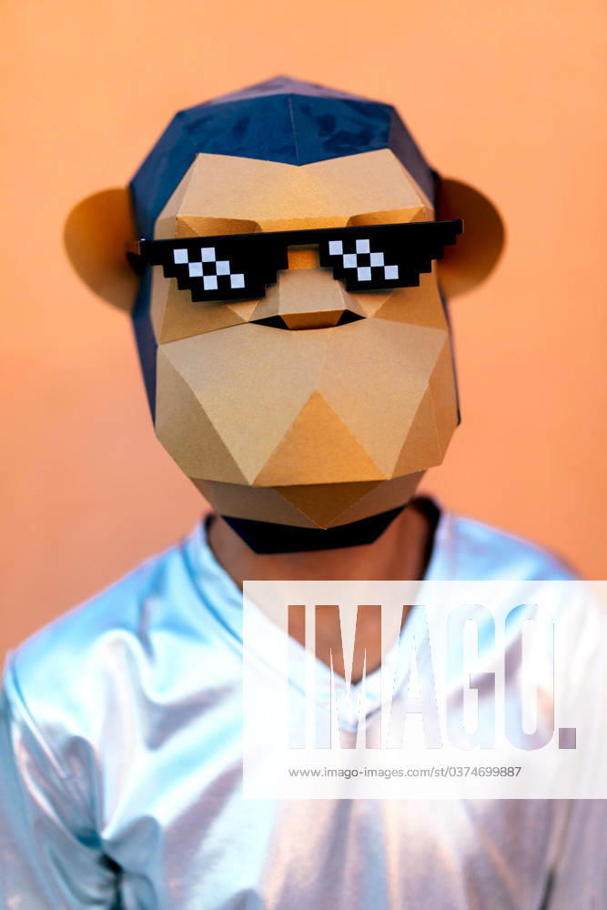 IMAGO Creative, Gesellschaft, Fasching Unrecognizable man in monkey mask standing against orange backdrop Anonymous male in silver V neck shirt and monkey mask with pixel party sunglasses looking at camera while standing against orange background in light Model Released SergioVictorVega_ID17382_528473_020