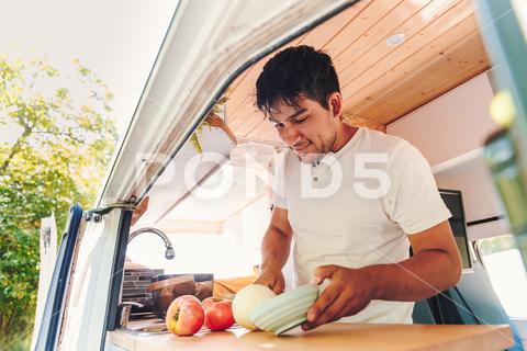 Young latin man cooking food in the kitchen of his handmade camper van. Van road trip holiday and outdoor summer adventure. Nomad lifestyle concept hispanic man cooking food camper van meal vanlife kitchen nomad lifestyle happy having great time good vibes young 30s male latin travel van life alternative vacation road nature handmade camping adventure trip holiday journey camper van summer motorhome tranquility tourism outdoor leisure campervan home road trip adventure travel freedom destination wanderlust wilderness mountain range rural open road latinx