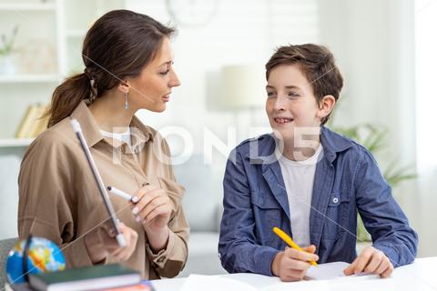 Home education, woman teaches boy at home sitting at table in living room, mother explains educational material to son doing homework together. studying woman home boy homework mother teacher teaching mentor tutor education eltern indoor son student person school cyberspace young laptop support smile computer adult together family childhood american online remote dining room task pupil assignment positive paper writing modern celebrate cognition lesson people high copybook learn project schoolkid browsing clever