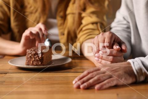 Romantic date. Couple holding hands together at table in cafe, closeup adult background beautiful bonding boyfriend cafe cake casual closeup couple date dating eat enjoying enjoyment family feelings female flirt focus food girlfriend hands holding indoors lifestyle love lovely lover lovers male man meet meeting people piece relationships restaurant romance romantic selective spending spoon sweetheart table time together togetherness woman wooden