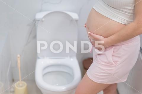 Pregnant woman holding her belly in the toilet. incontinence during pregnancy pregnant woman holding belly toilet incontinence during pregnancy pain care bathroom birth ache bladder childbirth constipation expecting fatigue hands cramp crotch control health healthcare hurt hurrying hygiene indigestion infection labor maternity mom mother pee pressure restroom problem rushing stomach suffer urgent urination weak home body symptom bad tummy