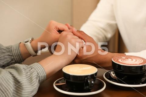 Romantic date. Couple holding hands together in cafe, closeup adult background biracial bonding boyfriend cafe cappuccino casual closeup coffee couple cups date dating drink enjoying enjoyment feelings female flirt girlfriend guy hands happiness holding indoors latte lifestyle love lovely lover lovers male man meeting mixed multiracial people relationships romance romantic spending sweetheart table time together togetherness woman young