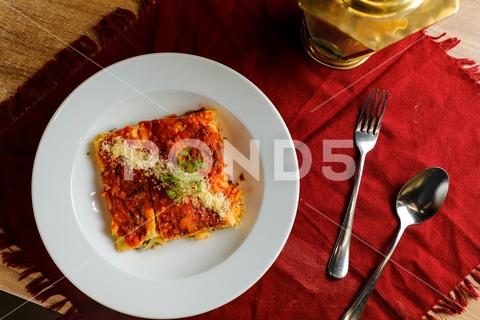 Spicy Tomato and Beef Lasagna served in plate with fork and spoon isolated on red napkin top view of fast food on table delicious spicy spaghetti rustic herb traditional piece lasagna meat beef tomato tomato and beef lasagna beef lasagna tomato lasagna baked meal dinner italian cooked pasta lasagne cheese vegetable sauce cuisine fresh dish basil serving portion food wooden homemade parmesan mediterranean restaurant golden plate lunch served isolated red napkin spoon fork table fast food top view