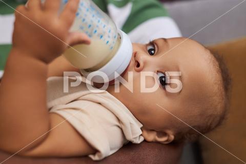 Close up portrait of adorable Black baby boy drinking milk or formula from bottle in fathers arms family Black father son boy dad little kid feeding bottle milk holding formula eating home love relationship Black man man bonding togetherness child development sitting sofa couch parent fatherhood single father African American cosy cozy lifestyle everyday life care affection bond connection happy happiness joy together cute childhood indoors