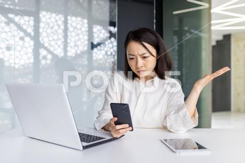 Upset sad woman at workplace holding smartphone, depressed business woman browsing social media inside office, Asian female worker using laptop at work. woman phone sad office mobile phone person problem upset mobile businesswoman employee business unhappy bad frustrated message online professional asian korean japanese chinese stress anxiety bankruptcy bank computer corporate depressed debt trouble looking closeup typing young job confused connection worried disappointed lost accountant thinking pressure manager annoyed executive money call
