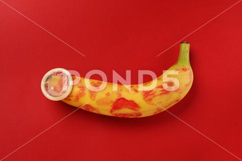 Banana with condom and lipstick marks on red background, top view. Safe sex concept abstract aids background banana birth care concept condom contraception control creative desire education erection erotic fetish food fresh fruit game genital health infection intercourse intimacy kiss latex love lovers male man object oral orgasm passion penis pleasure porn potency prevention protection red rubber safe satisfaction sex sexual symbol top view