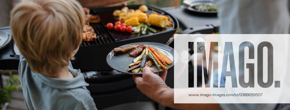 Father putting grilled meat and vegetable on plate to his son during family summer garden party. A father putting grilled meat and vegetable on plate to his son during family summer garden party. model released