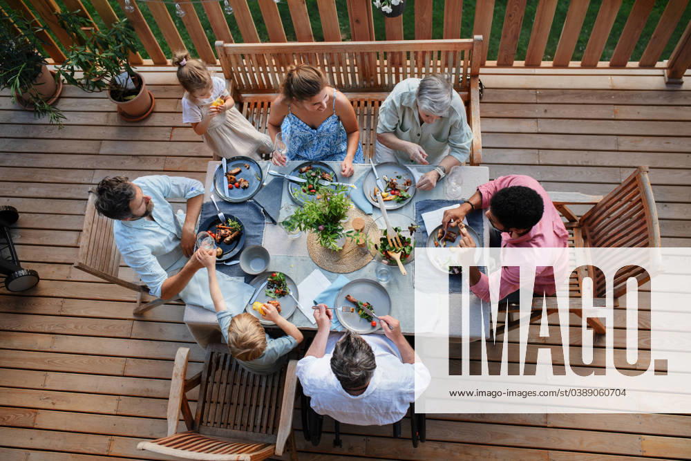Top view of 3 generations family eating at barbecue party dinner on patio, people sitting at table on patio with grill. A top view of 3 generations family eating at barbecue party dinner on patio, people sitting on patio with grill. model released
