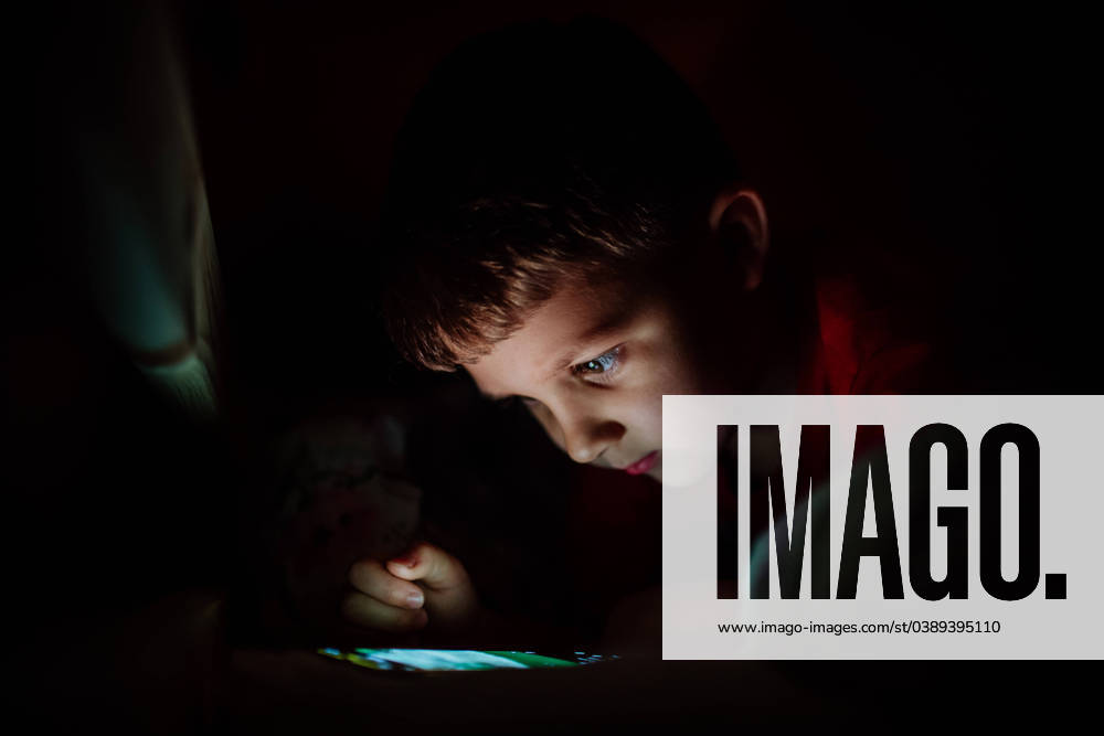 Addicted little boy playing games on phone in bed at night. An addicted little boy playing games on phone in bed at night. model released