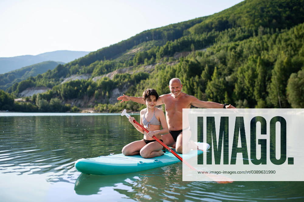 Happy preteen girl with grandfather on summer holiday by lake, paddleboarding. A happy preteen girl with grandfather on summer holiday by lake, paddleboarding. model released