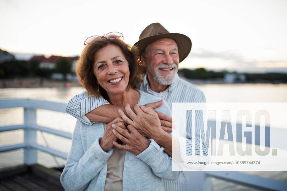 Happy senior couple hugging outdoors on pier by sea, looking at camera. A happy senior couple hugging outdoors on pier by sea, looking at camera. model released