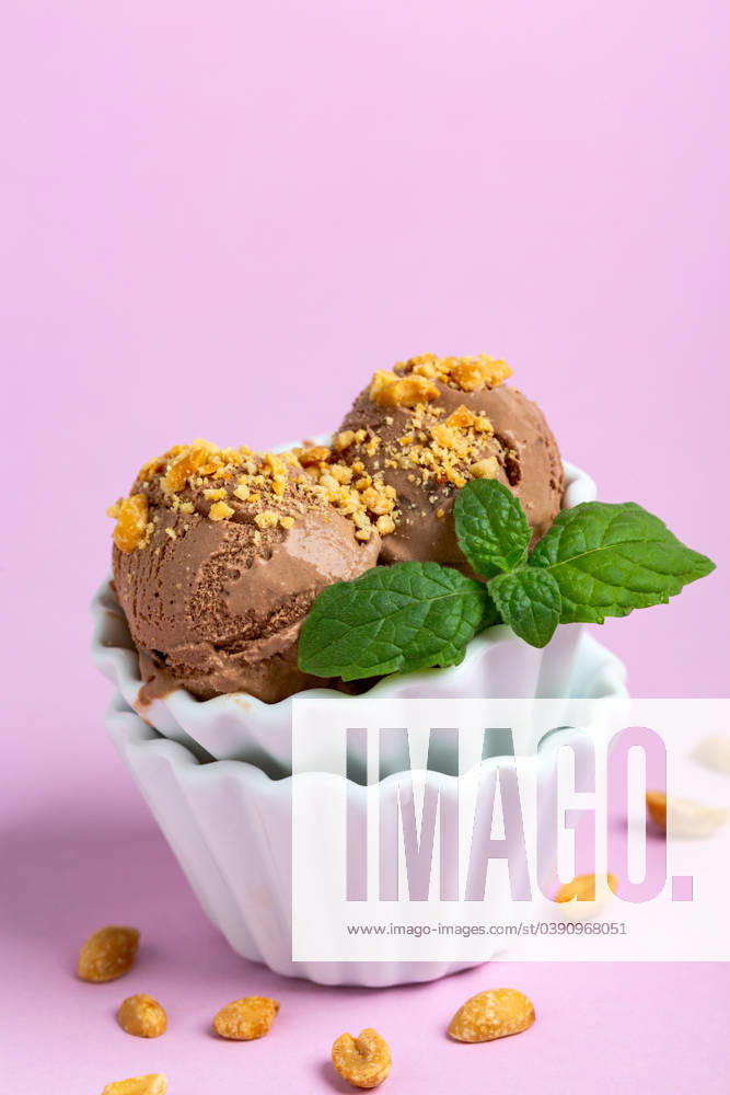 Chocolate ice cream balls with peanuts. Homemade chocolate ice cream with peanuts in a porcelain bowl with a sprig of mint on a pink background, selective focus.