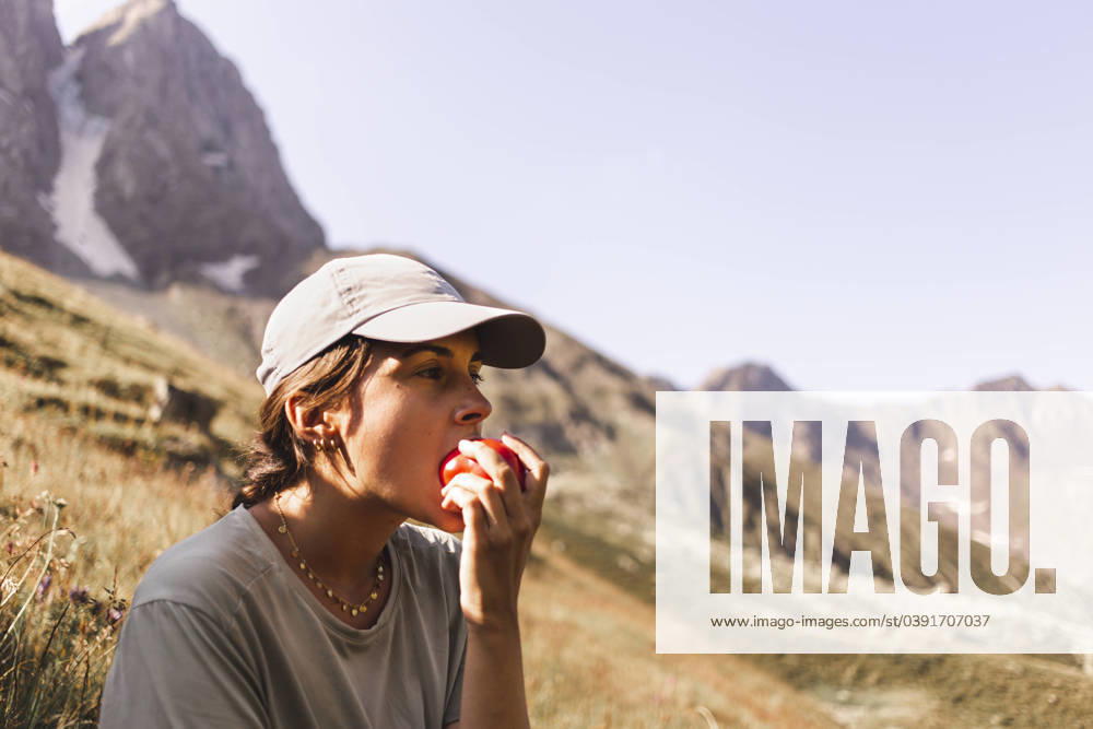 Woman wearing cap and eating tomato in front of mountains on sunny day model released, Symbolfoto, PCLF00956