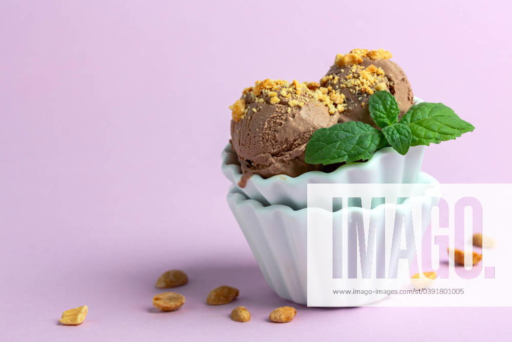 Chocolate ice cream balls with peanuts. Homemade chocolate ice cream with peanuts in a porcelain bowl with a sprig of mint on a pink background, selective focus.