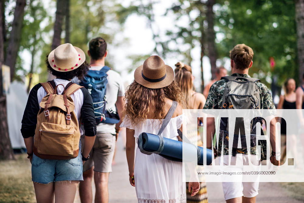 Rear view of group of young friends with backpack walking at summer festival. Rear view of group of young friends with backpack and mat walking at summer festival. model released